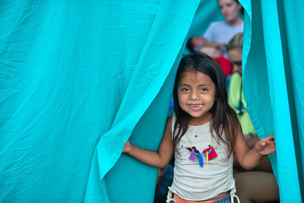 A girl smiles between turquoise curtains.